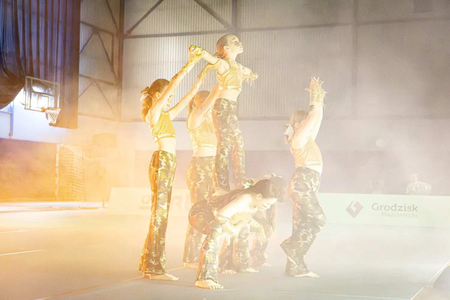 Grupa tancerek w strojach scenicznych podczas układu choreograficznego w hali sportowej.